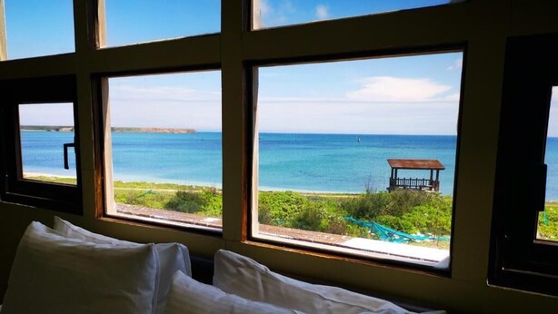 A room with a bed and large windows overlooking a beach with a gazebo. - 23.5 Blue B & B (Xiyu)
