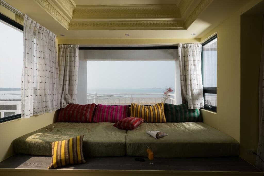A room with a large window, a sofa with colorful cushions, and a view of the sea.