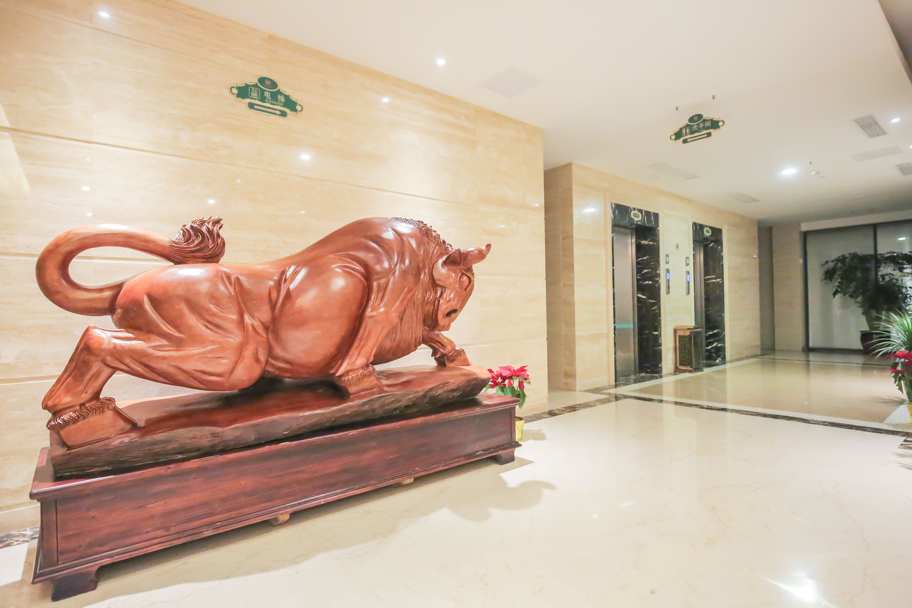 A lobby with a wooden bull sculpture, elevators, and a polished floor.