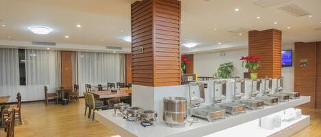 Zona de comedor de hotel con bufé, que incluye varios dispensadores de alimentos y un espacio de estar con mesas y sillas.