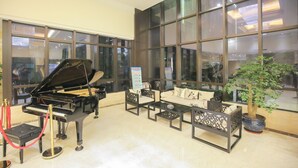 A grand piano, a sofa set, and a potted plant in a spacious lobby with large windows. - New Knight Royal Hotel (Shanghai)