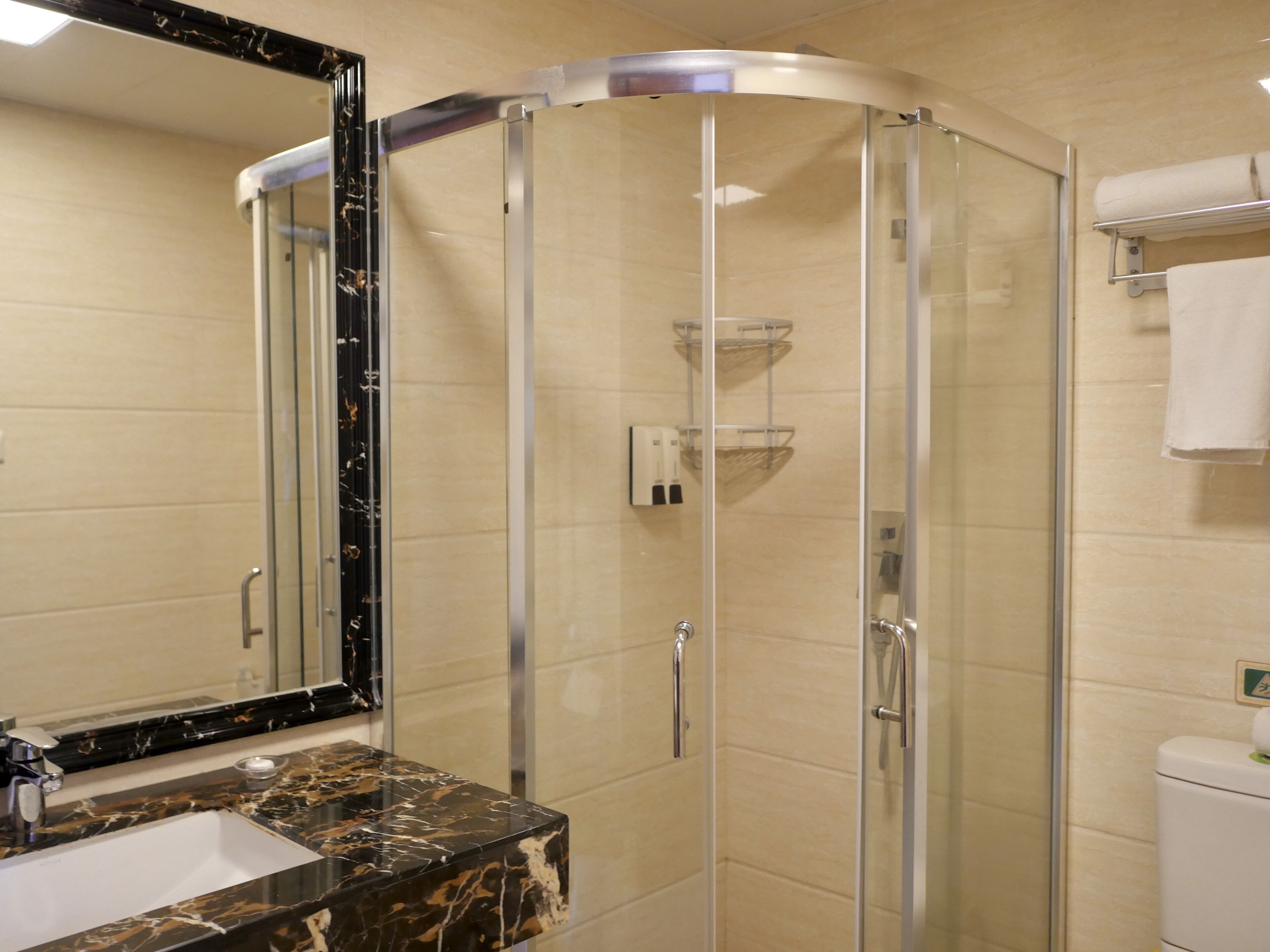 Un baño moderno con ducha de vidrio, lavamanos de mármol y un inodoro con toallero.