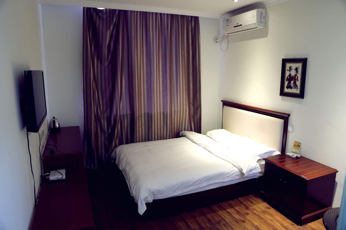 Une chambre d’hôtel avec un lit, une table de chevet, une télévision et un rideau.