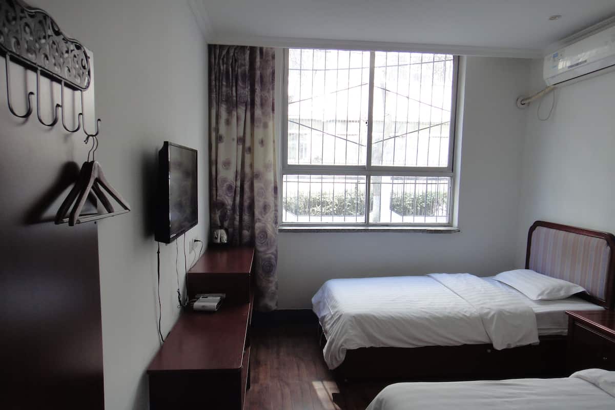 Une chambre avec deux lits, une télévision, un bureau et une fenêtre avec des rideaux.