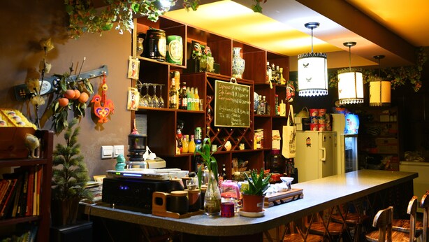 Un espace bar avec des étagères remplies de bouteilles, un menu écrit à la craie et un réfrigérateur.