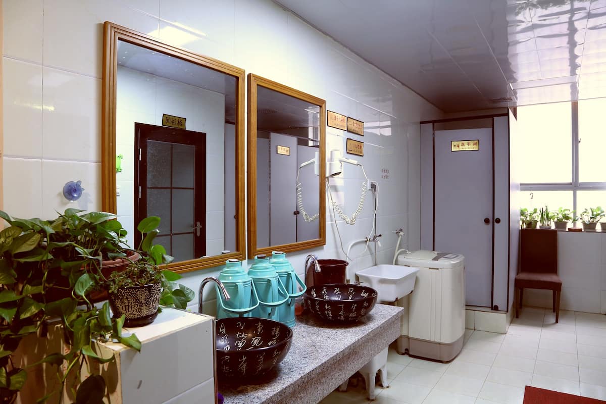 Une salle de bain avec un grand miroir, plusieurs lavabos, des toilettes et des plantes en pot.