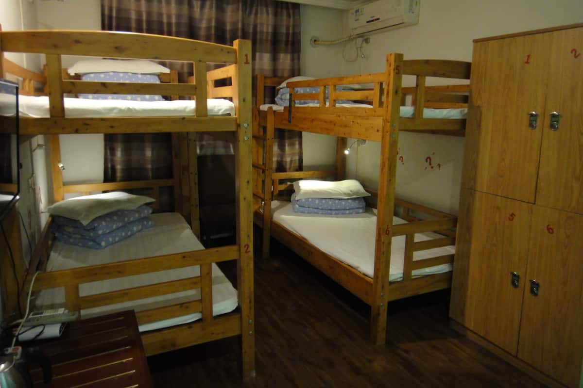 Une chambre avec des lits superposés en bois, une armoire et un appareil de climatisation fixé au mur.