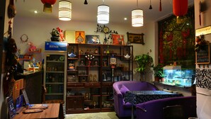 Une pièce avec un canapé violet, une table en bois et un aquarium. On y trouve des étagères remplies de divers objets, et une lanterne rouge suspendue au plafond.