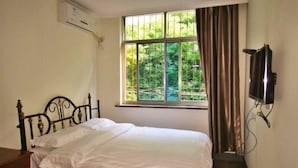 Une chambre avec un lit, une fenêtre avec des rideaux, un appareil de climatisation et un téléviseur fixé au mur.