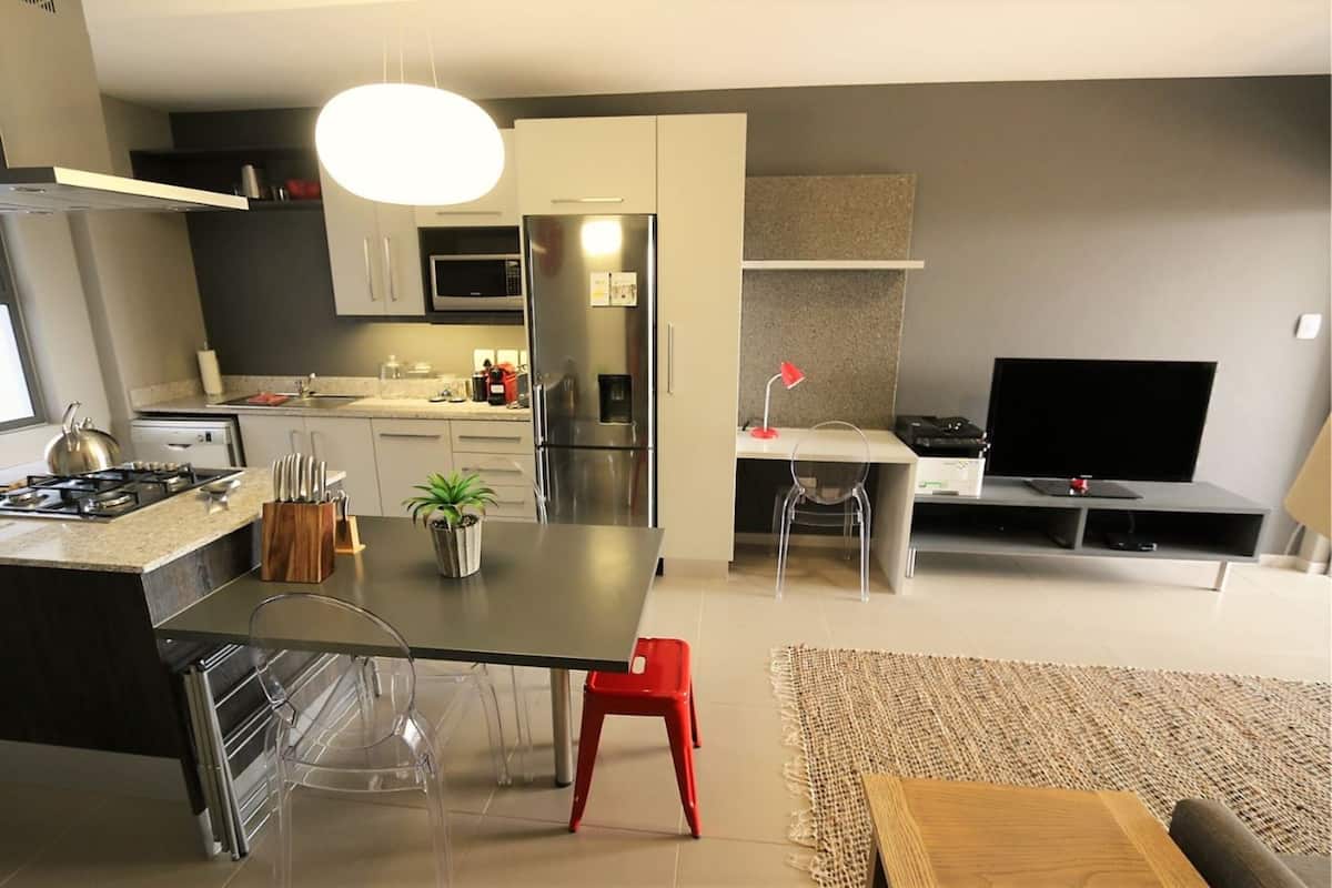 A modern kitchen with a central island, stainless steel appliances, and a dining area with a TV and seating.