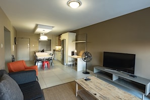 A modern living room with a sofa, TV, and a dining area with chairs and a table. - The Hub (Sandton)