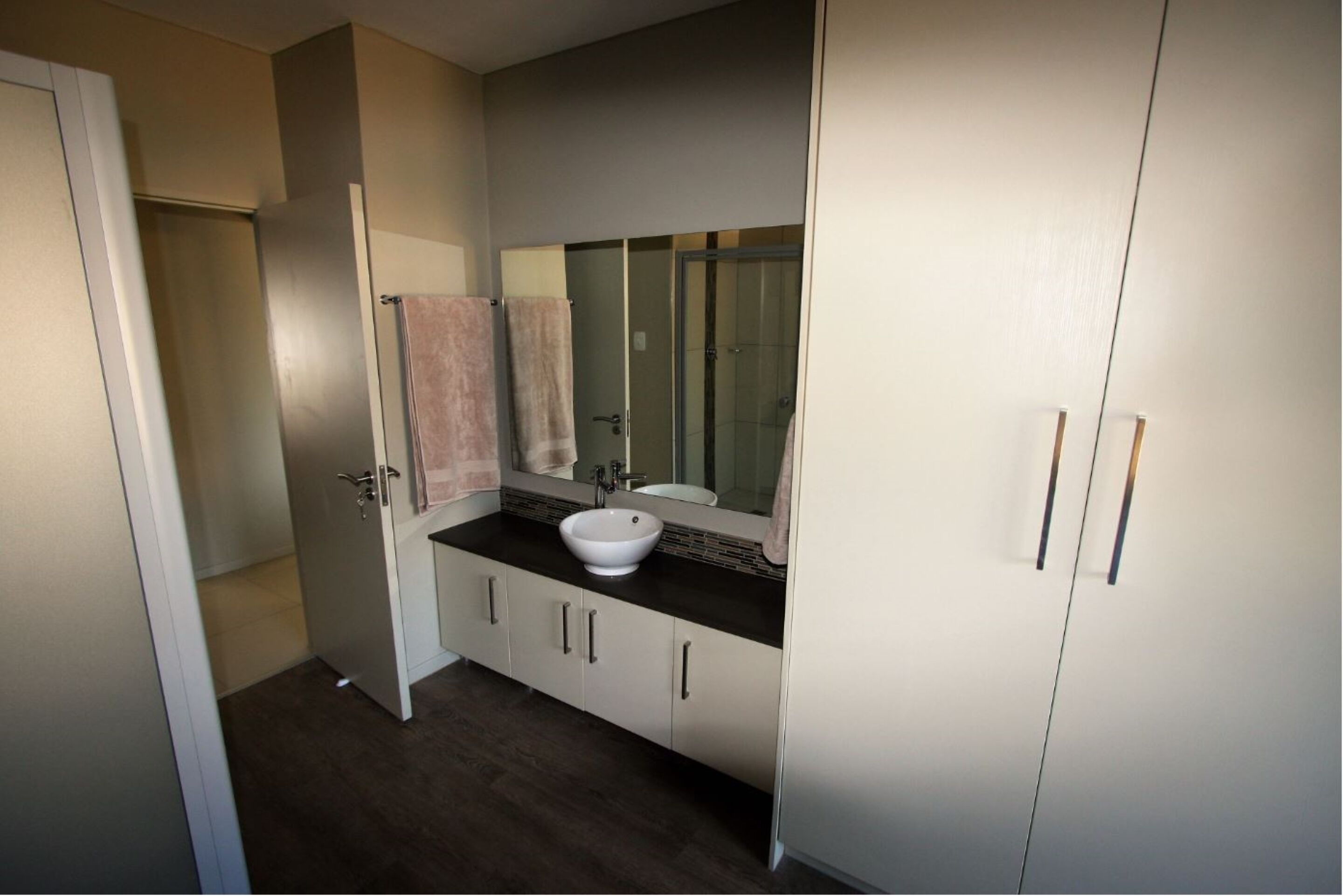 A bathroom with a white sink, a large mirror, and a beige cabinet.