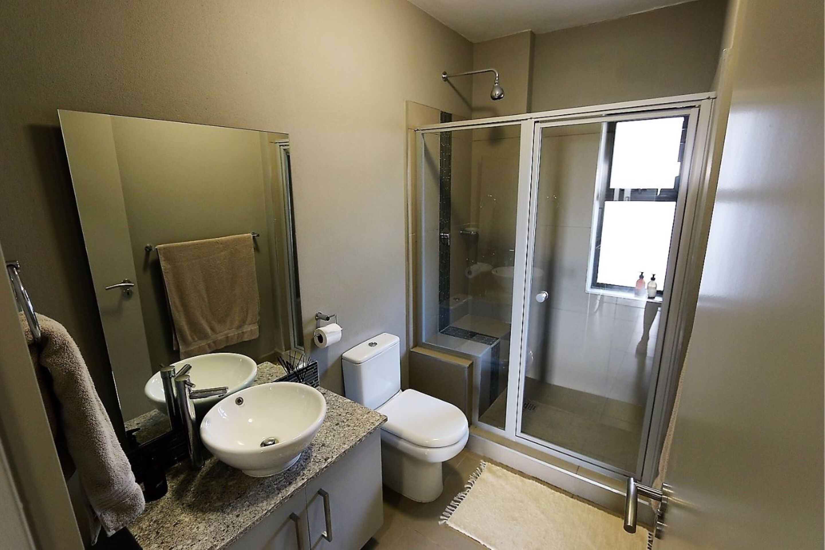 A modern bathroom with a glass-enclosed shower, a sink with a mirror, and a toilet.