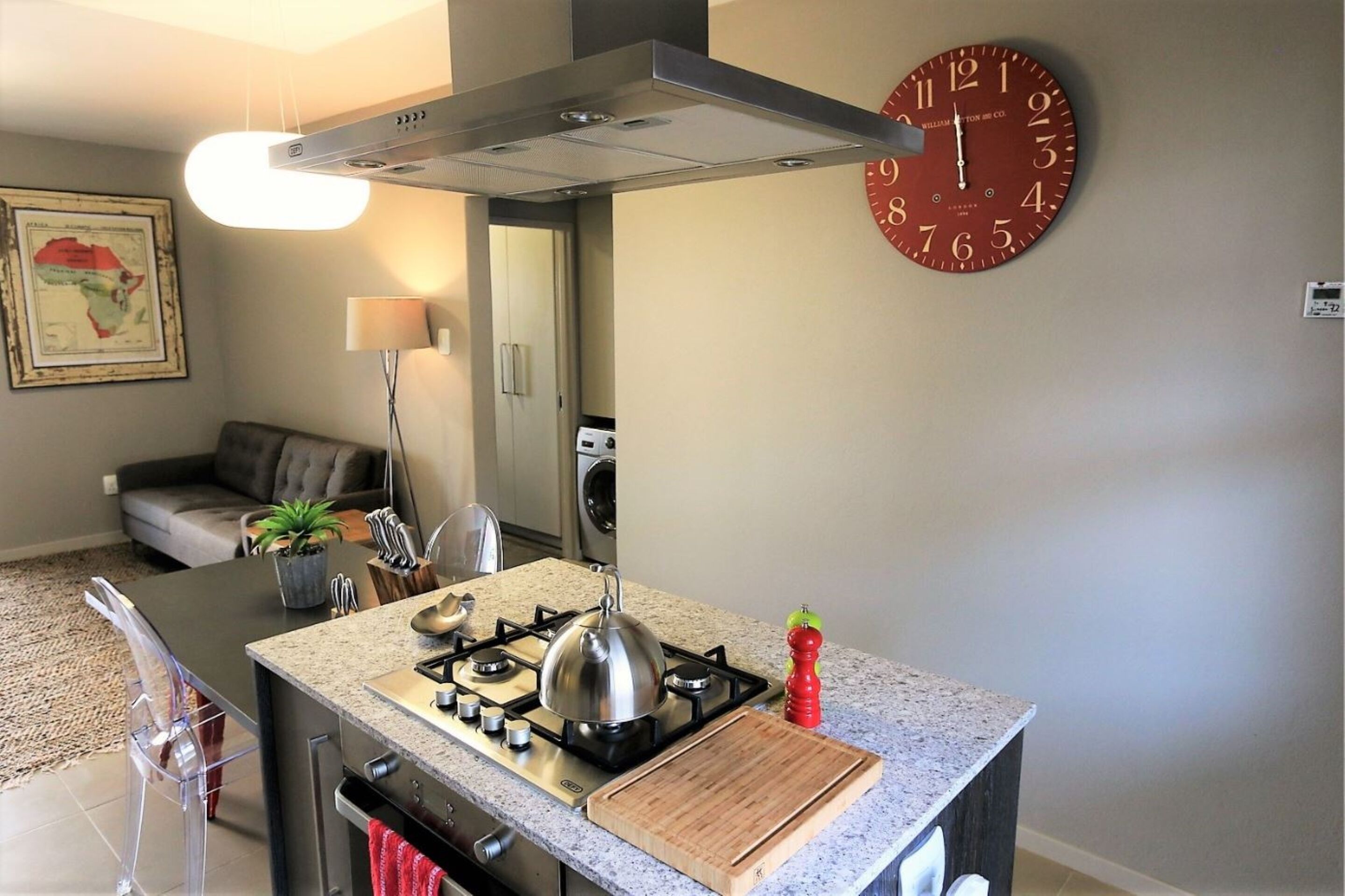 A compact kitchen with a gas stove, a kettle, and a cutting board.