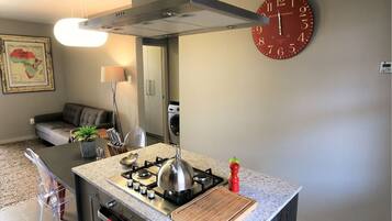 A compact kitchen with a gas stove, a kettle, and a cutting board.