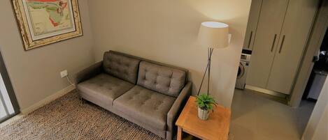 A living room with a sofa, a lamp, a small table with a plant, and a framed map on the wall.