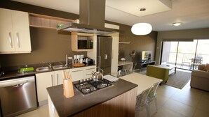 A modern kitchen with a central island, stainless steel appliances, and a dining area with a green chair.