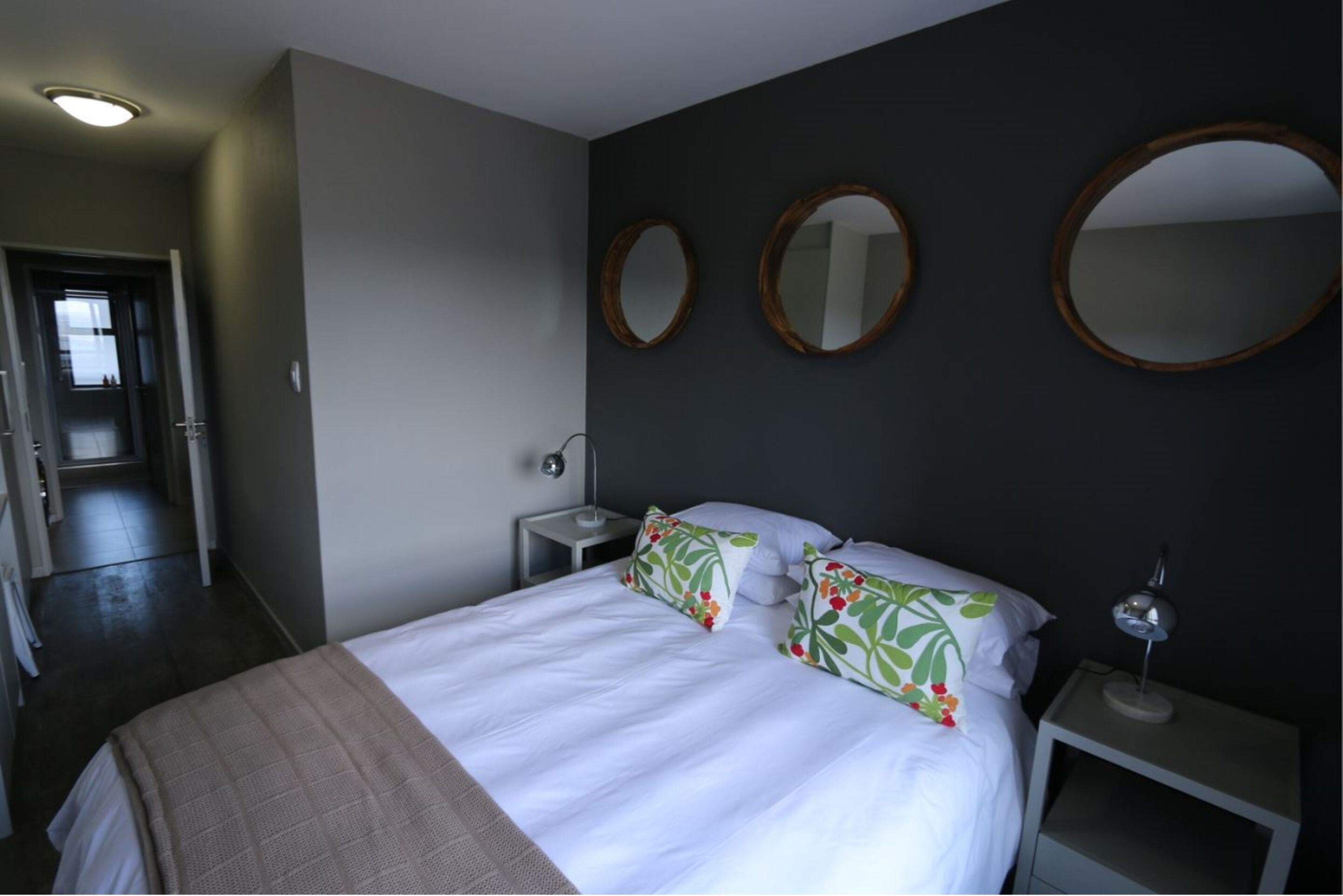 Et hotelværelse med en seng, to sengeborde, en lampe og tre spejle på væggen.