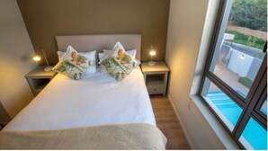 A neatly made bed with floral pillows, two bedside tables with lamps, and a large window with a view of greenery.