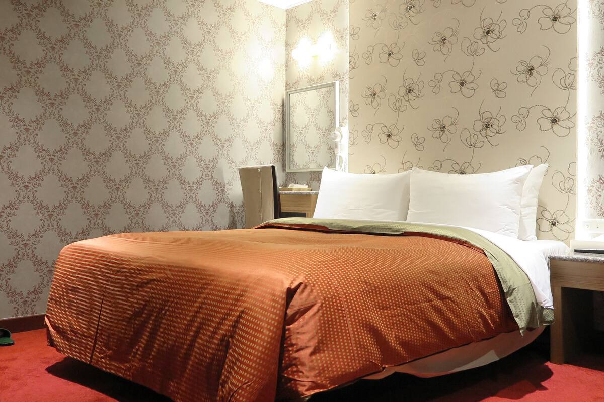Een hotelkamer met een bed, nachtkastje, spiegel en een bloemenbehang wand.