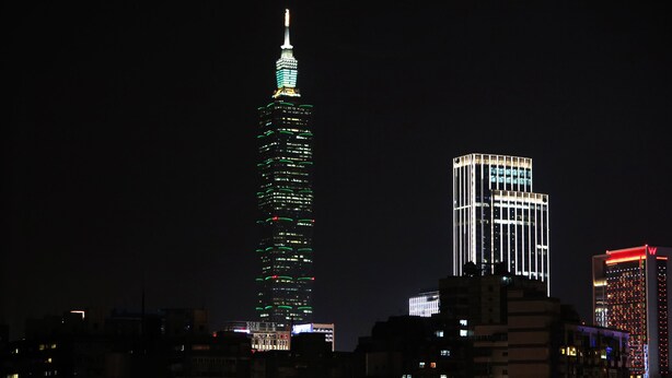 A cityscape at night with illuminated skyscrapers, including a prominent tower with green lights and another with white lights. - Nice Hotel (Taipei)