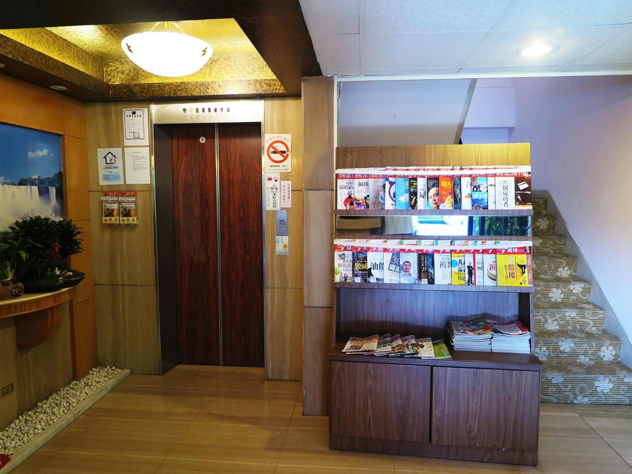A reception area with a wooden floor, a reception desk, a staircase, and a display of magazines.