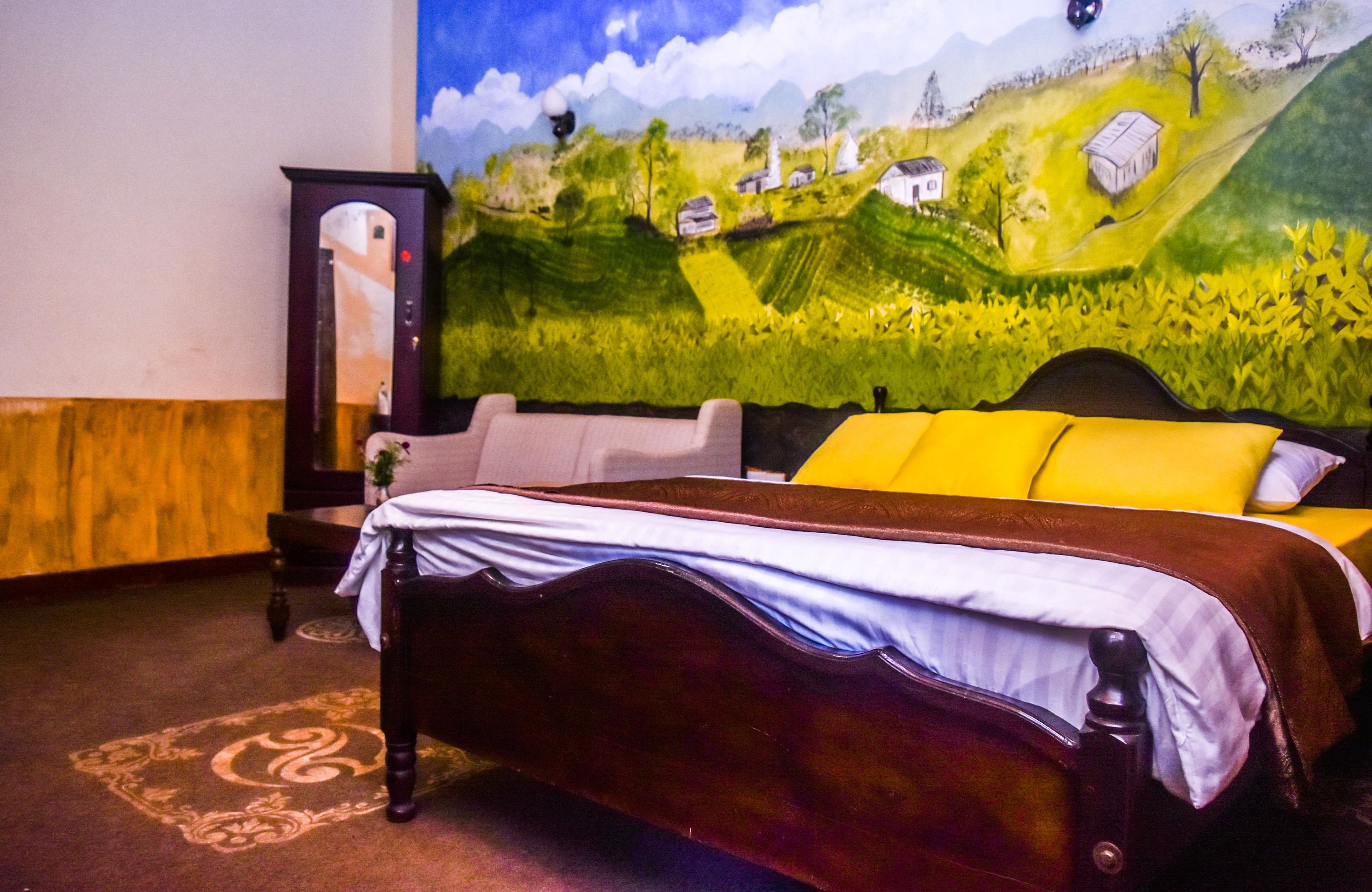 Un lit avec un cadre en bois et une couvre-lit blanche et marron, un oreiller jaune et une fresque murale représentant un paysage verdoyant.