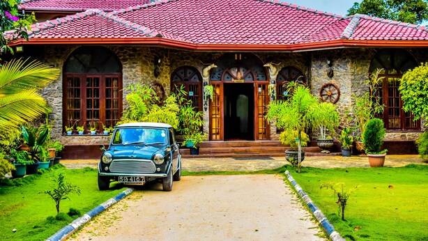 A stone house with a red-tiled roof, a vintage car parked in front, and a well-maintained garden. - MF Estate Holiday Bungalow (Hali-Ela)