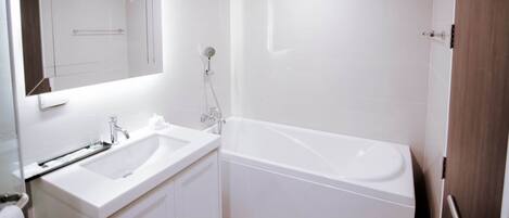 Un baño moderno con lavamanos, espejo y bañera blancos.