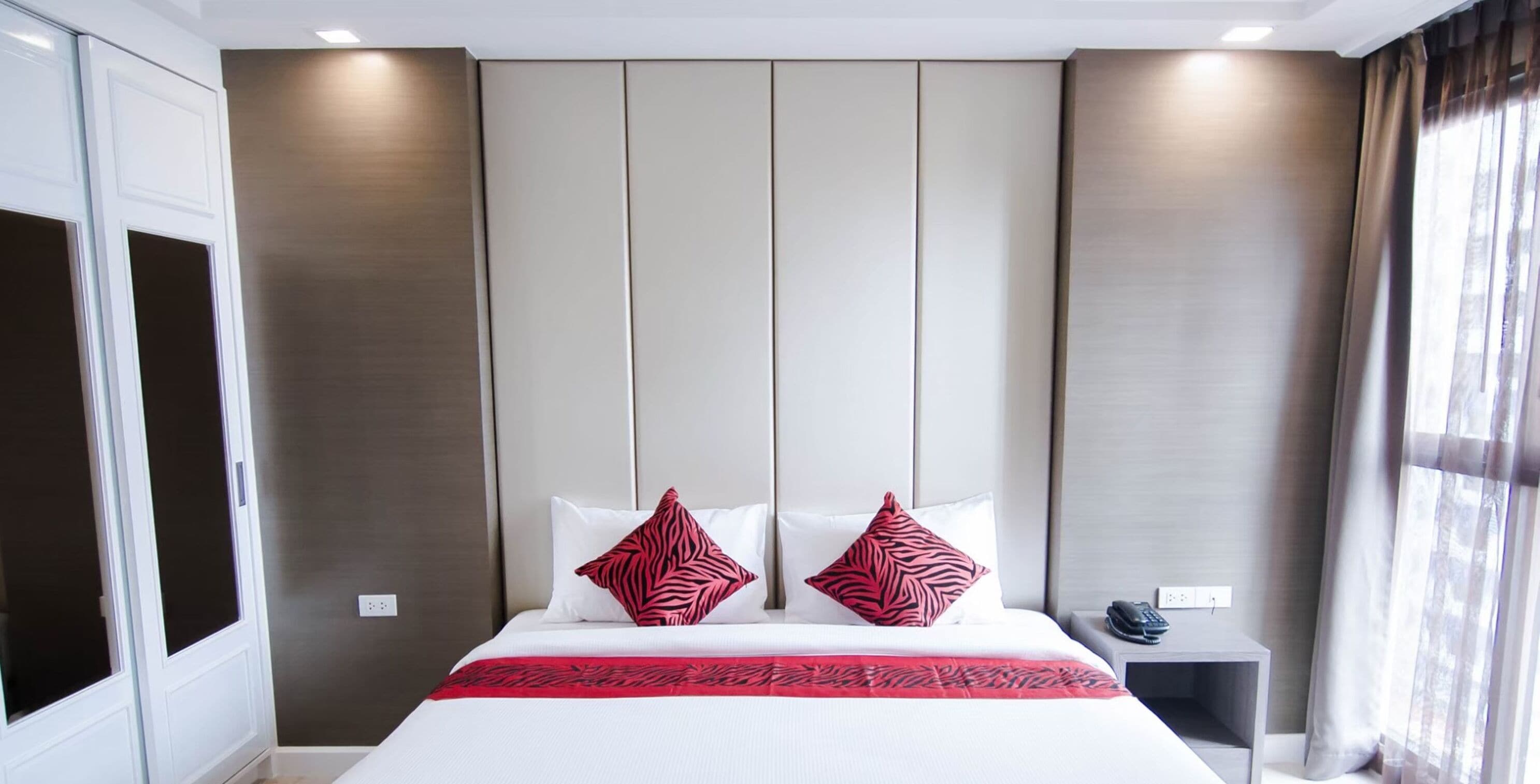 Una habitación de hotel con una cama grande, dos almohadas, una mesita de noche con un teléfono y una ventana con cortinas.