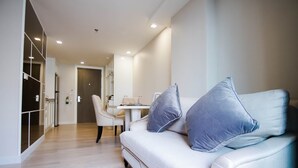 Un salon moderne comprenant un canapé, deux coussins, une table à manger avec des chaises et un couloir menant à une porte.