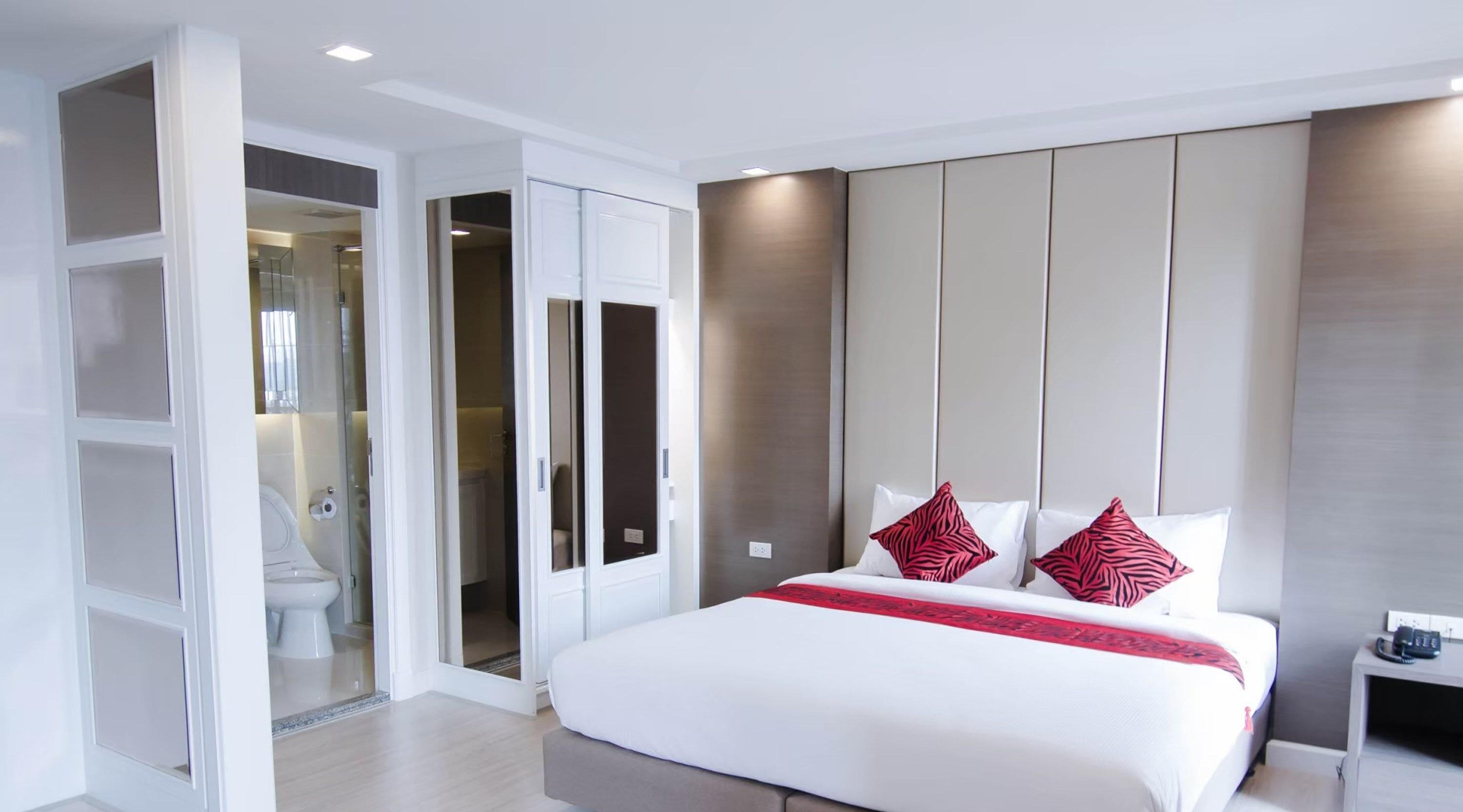 Ein modernes Hotelzimmer mit einem großen Bett, einem begehbaren Kleiderschrank und einem Badezimmer mit Glasabtrennung.