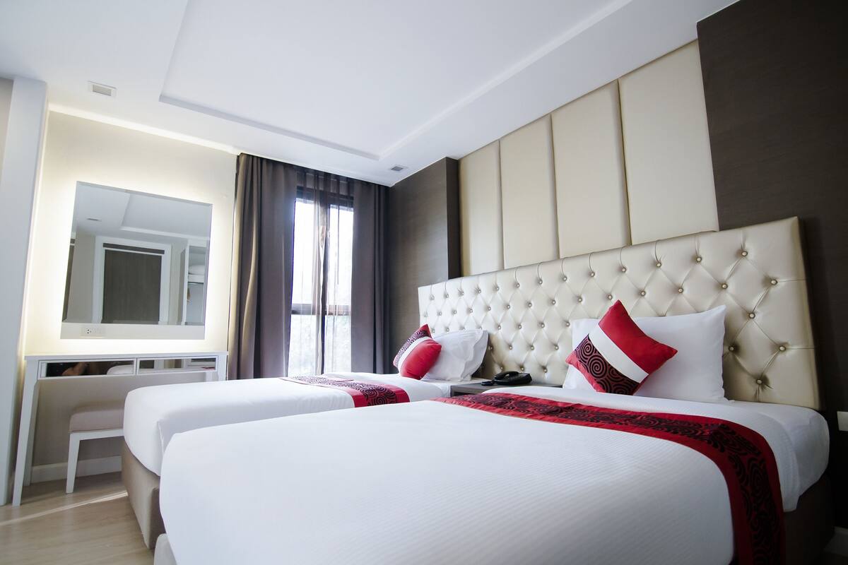 Quarto de hotel com duas camas, uma escrivaninha e um espelho grande.