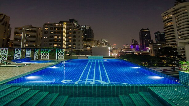 Une piscine sur le toit, au design géométrique, entourée de gratte-ciel et illuminée par les lumières de la ville.