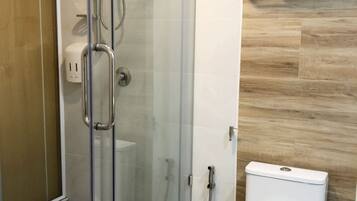 Un baño moderno con ducha de cristal, inodoro blanco y suelo de madera.