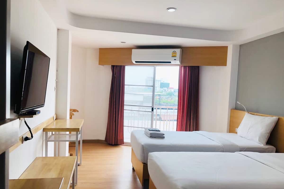 A hotel room with two beds, a TV, a desk, and an air conditioning unit.