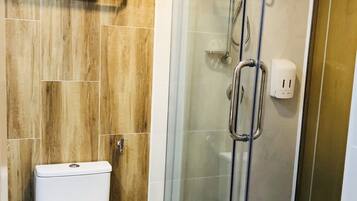A modern bathroom with a toilet, a glass shower enclosure, and a wooden wall.