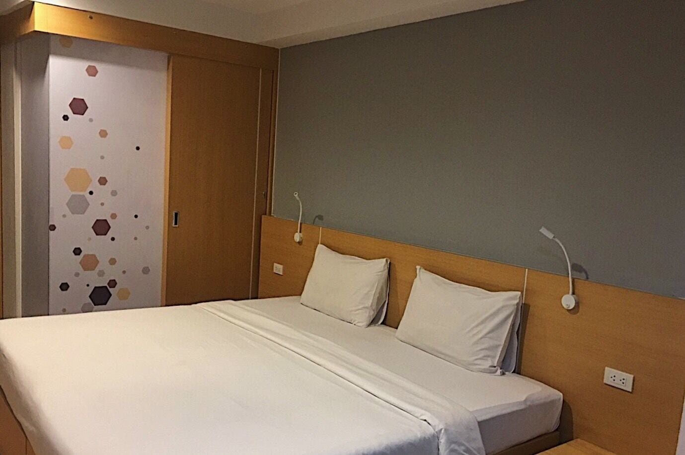 Habitación de hotel con cama, dos mesitas de noche, un armario y una pared con diseño geométrico.