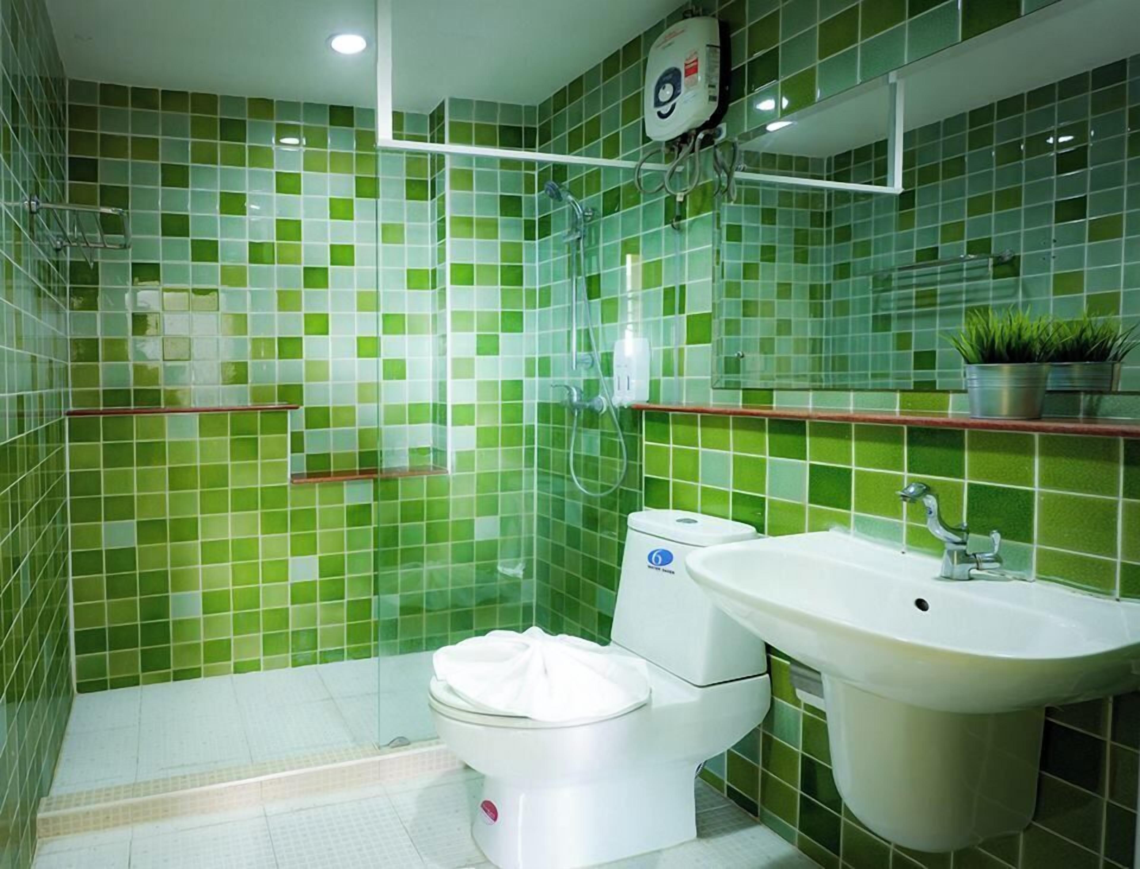 Un baño con mosaicos verdes, un inodoro blanco, un lavabo y una ducha.