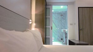 Moderni hotellihuone, jossa on suuri sänky, puinen pääty ja marmoriseinäinen kylpyhuone sekä ovi, joka johtaa toiseen huoneeseen.