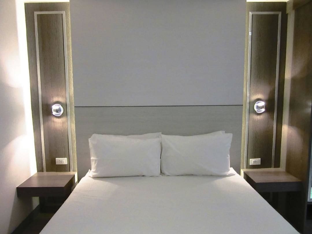 A hotel room with a large bed, two bedside tables, and wall-mounted lighting.