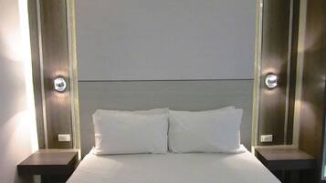 A hotel room with a large bed, two bedside tables, and wall-mounted lighting.