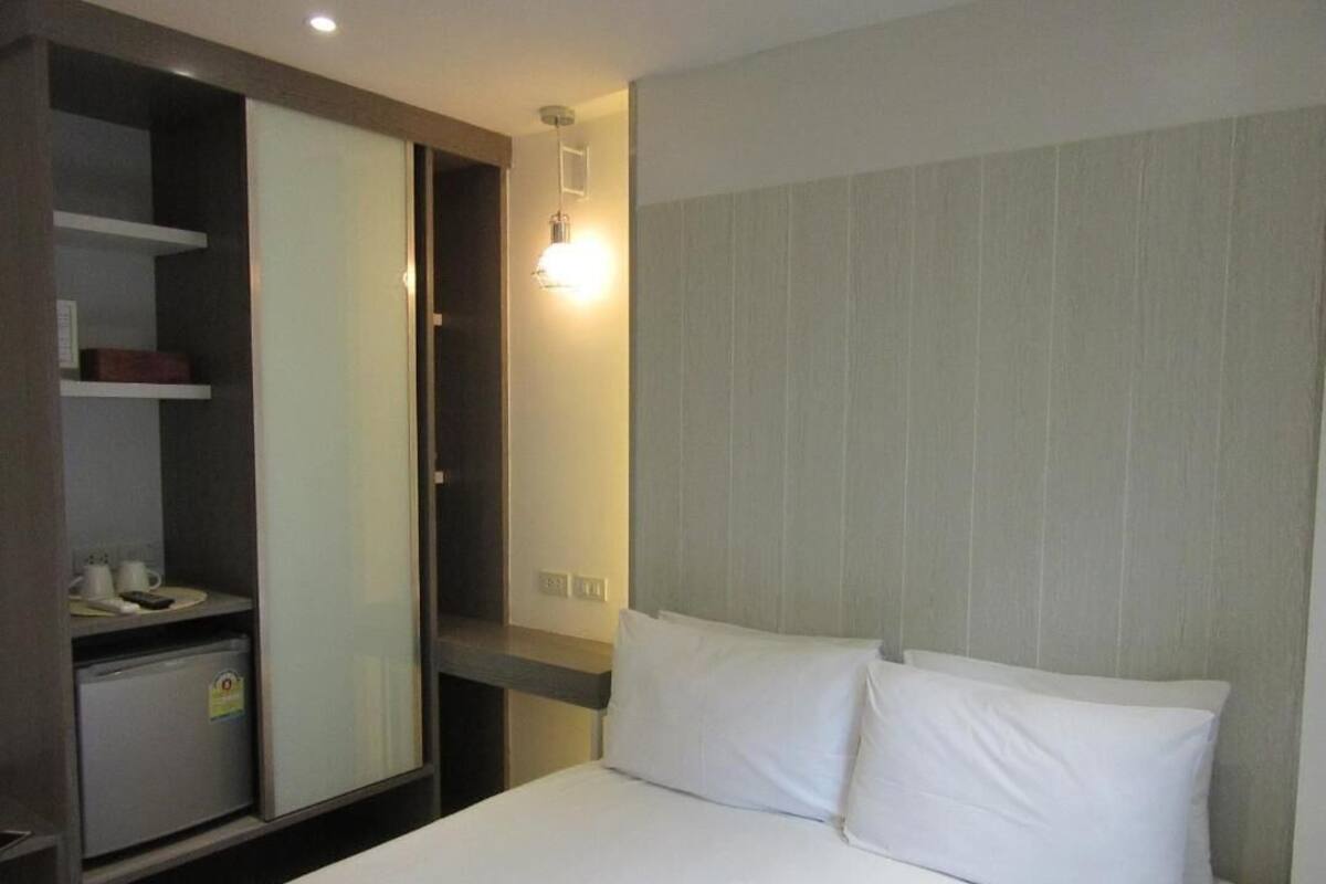 A hotel room with a bed, a wardrobe, and a small desk with a lamp.