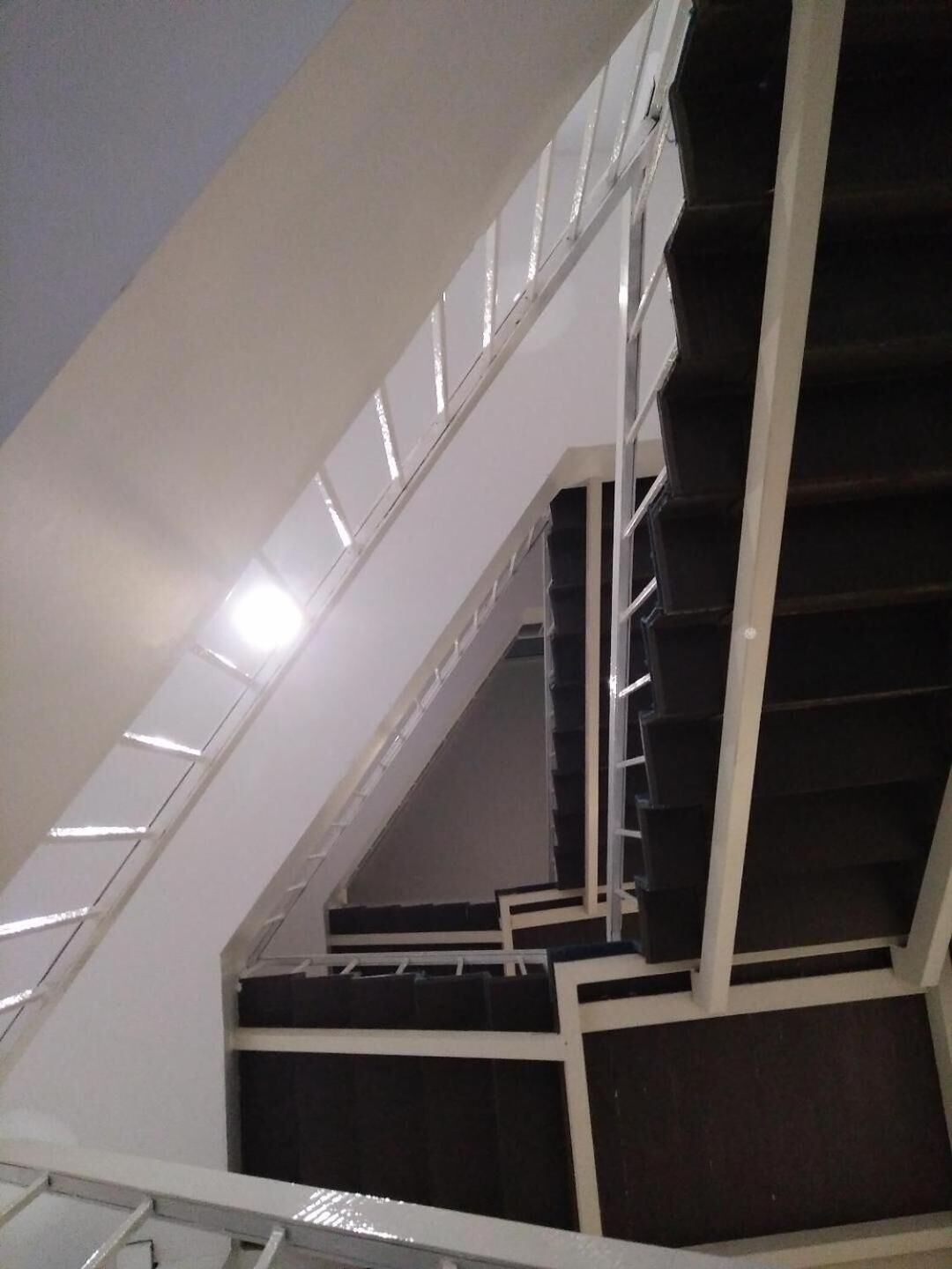 A staircase with white railings and dark steps, leading to an upper floor.