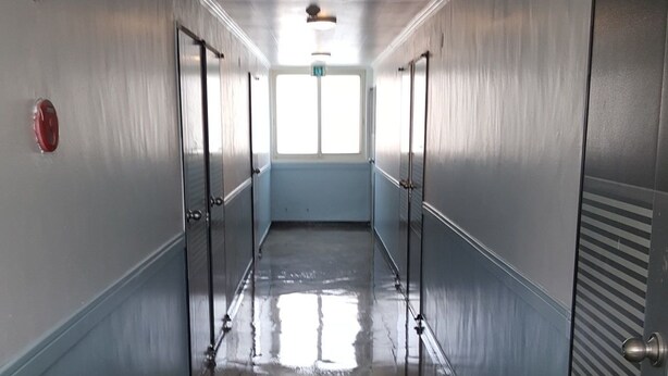 A long, narrow hallway with a shiny floor, doors on both sides, and a green exit sign on the ceiling. - MK Guest House (Busan)