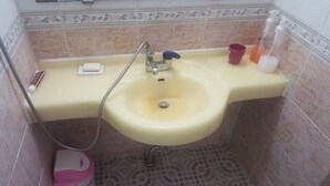 A bathroom with a yellow sink, a handheld showerhead, a soap dish, and a few toiletries on the counter. - MK Guest House (Busan)