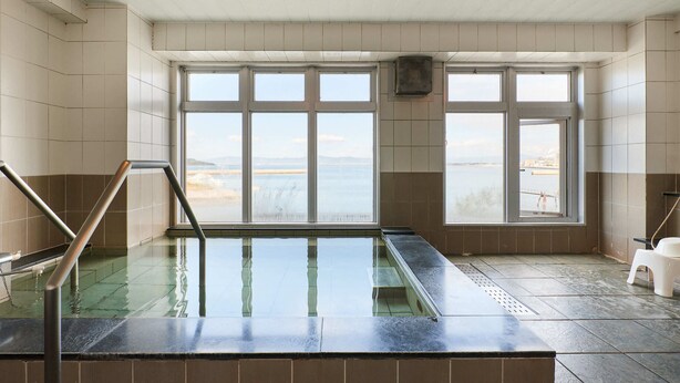 Ein Wellnessbereich mit einem großen, gläsernen Whirlpool, Meerblick und einem weißen Kunststoffhocker.