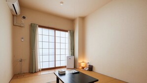 Ein Zimmer mit Tatami-Böden, einer schiebbaren Shoji-Schiebetür, einem Tisch mit Fernbedienung, einem Heizgerät und einer Lampe.