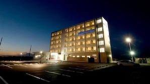 Ein mehrstöckiges Gebäude mit beleuchteten Fenstern bei Nacht, ein Parkplatz und eine Straßenlaterne.