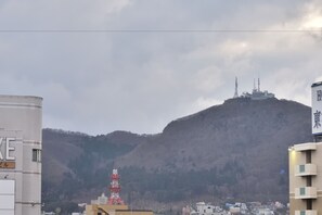 A cityscape with a prominent hill in the background, featuring a telecommunications tower and a building with antennas. - A-Gate Hotel (Hakodate)